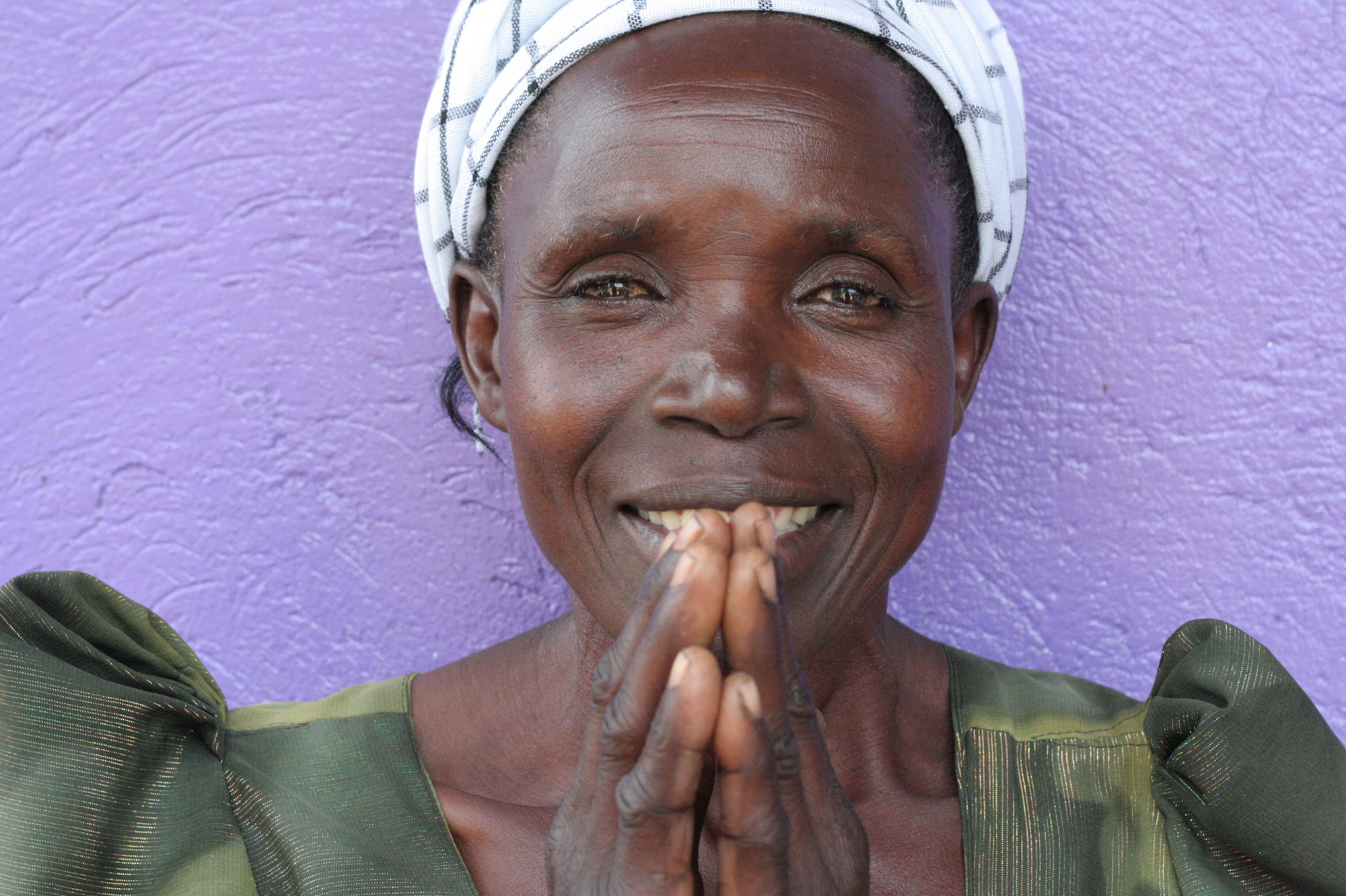 Woman in front of a purple wall with her hands raised as in prayer