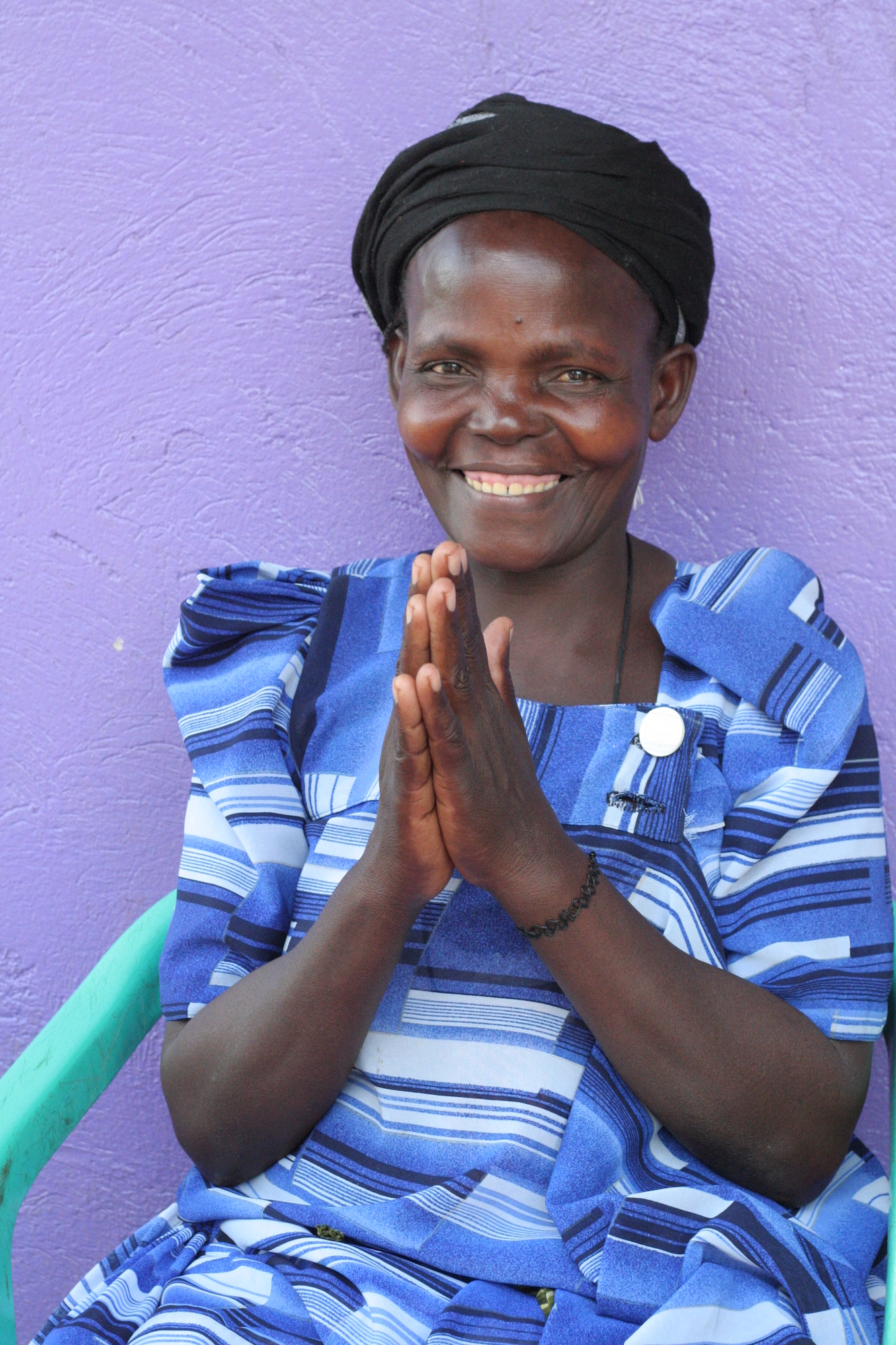 Woman smiling in front of a purple wall with hands raised as in prayer