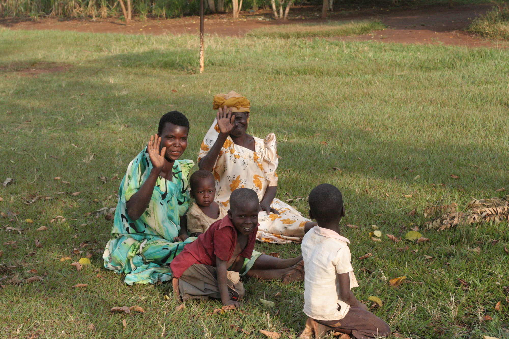 Women & children sitting on the grass, waving at the camera