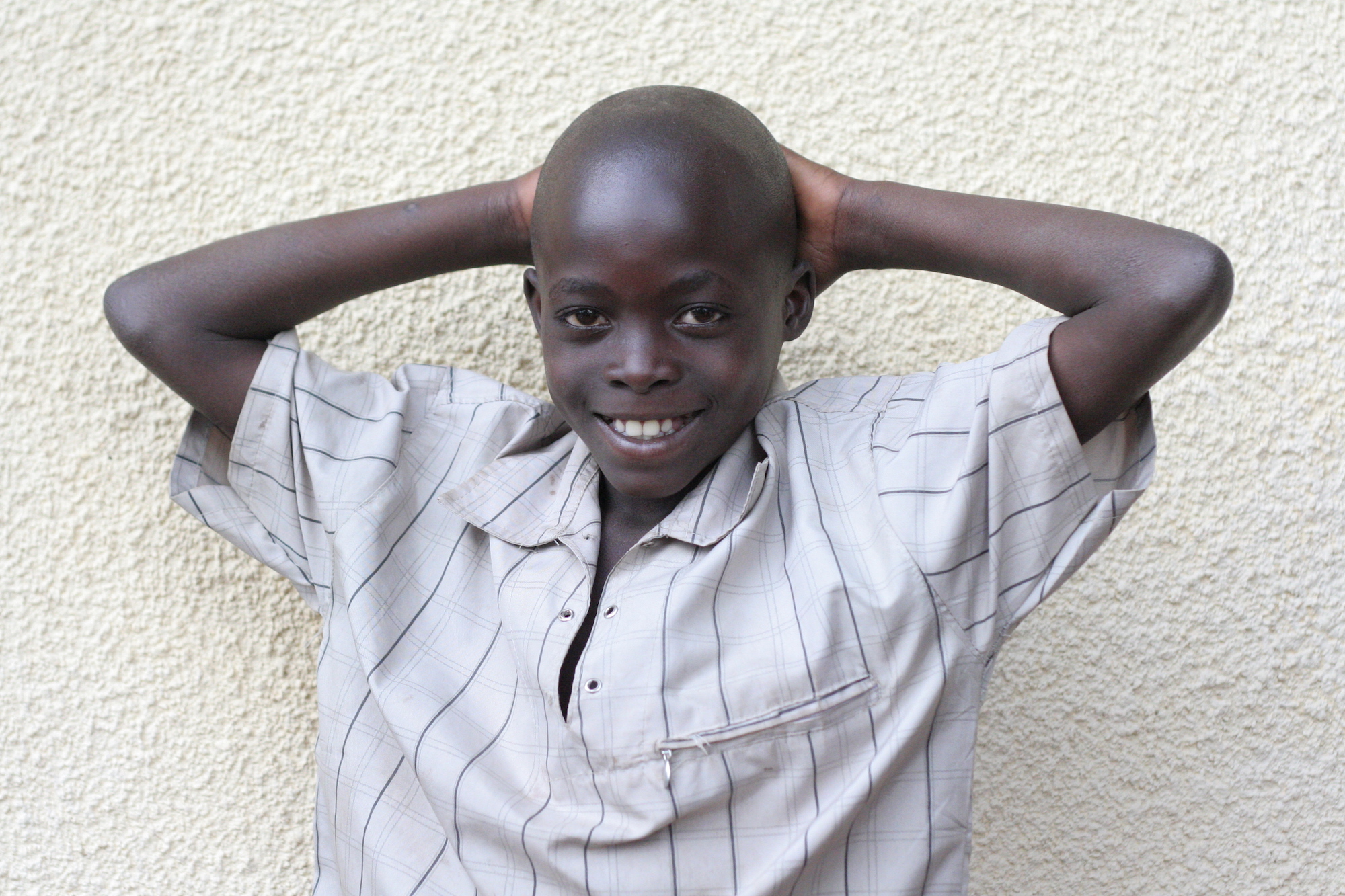 Boy smiling in front of a wall with his hands behind his head