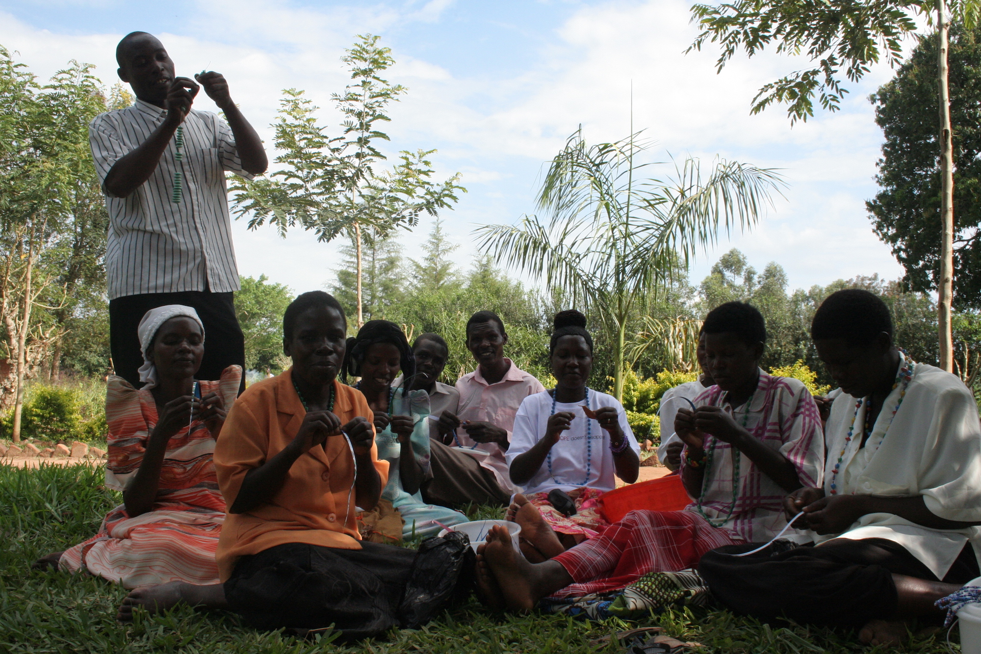 Group of people sitting in the grass making beads