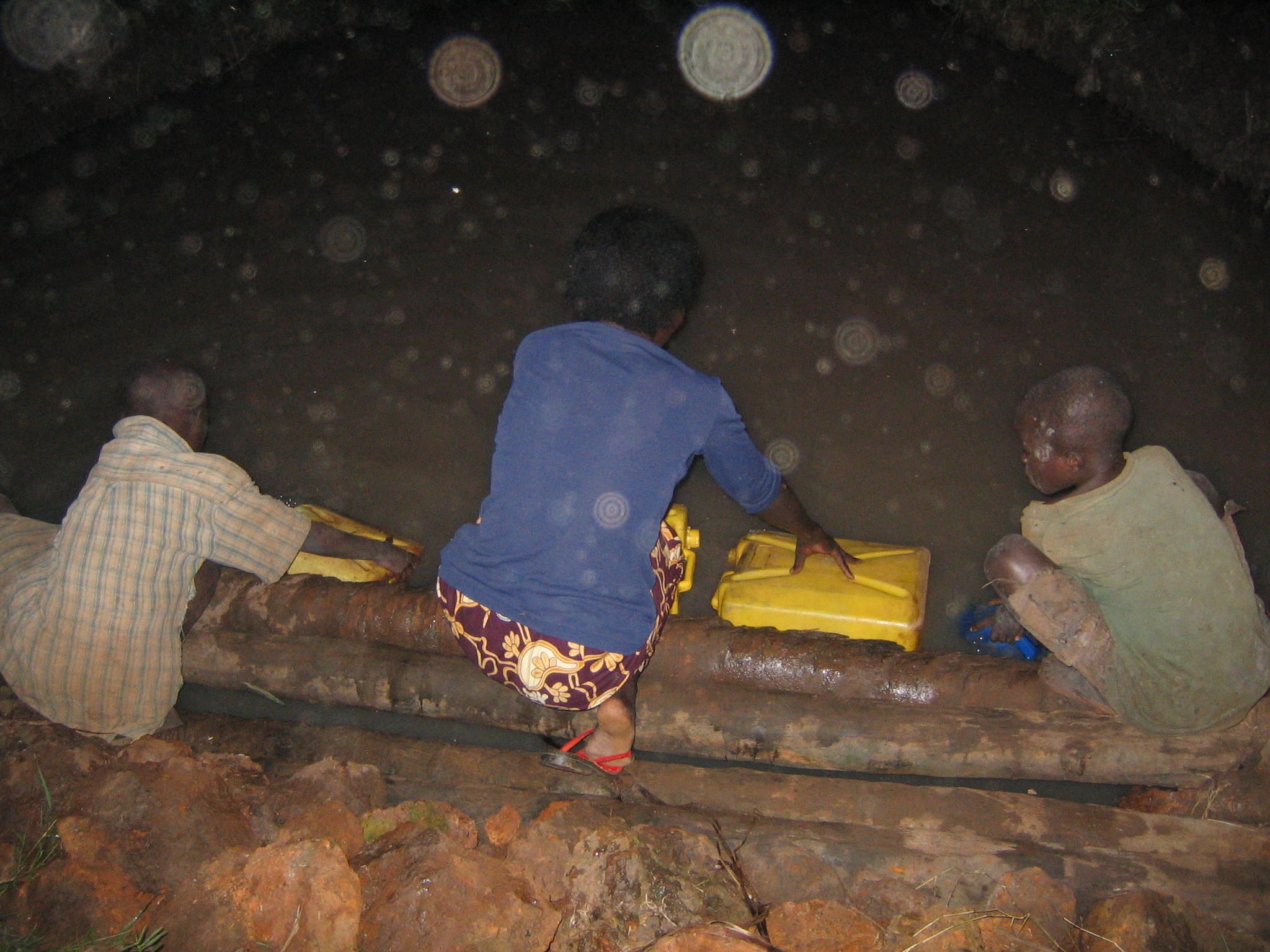 Three people taking water from a well.