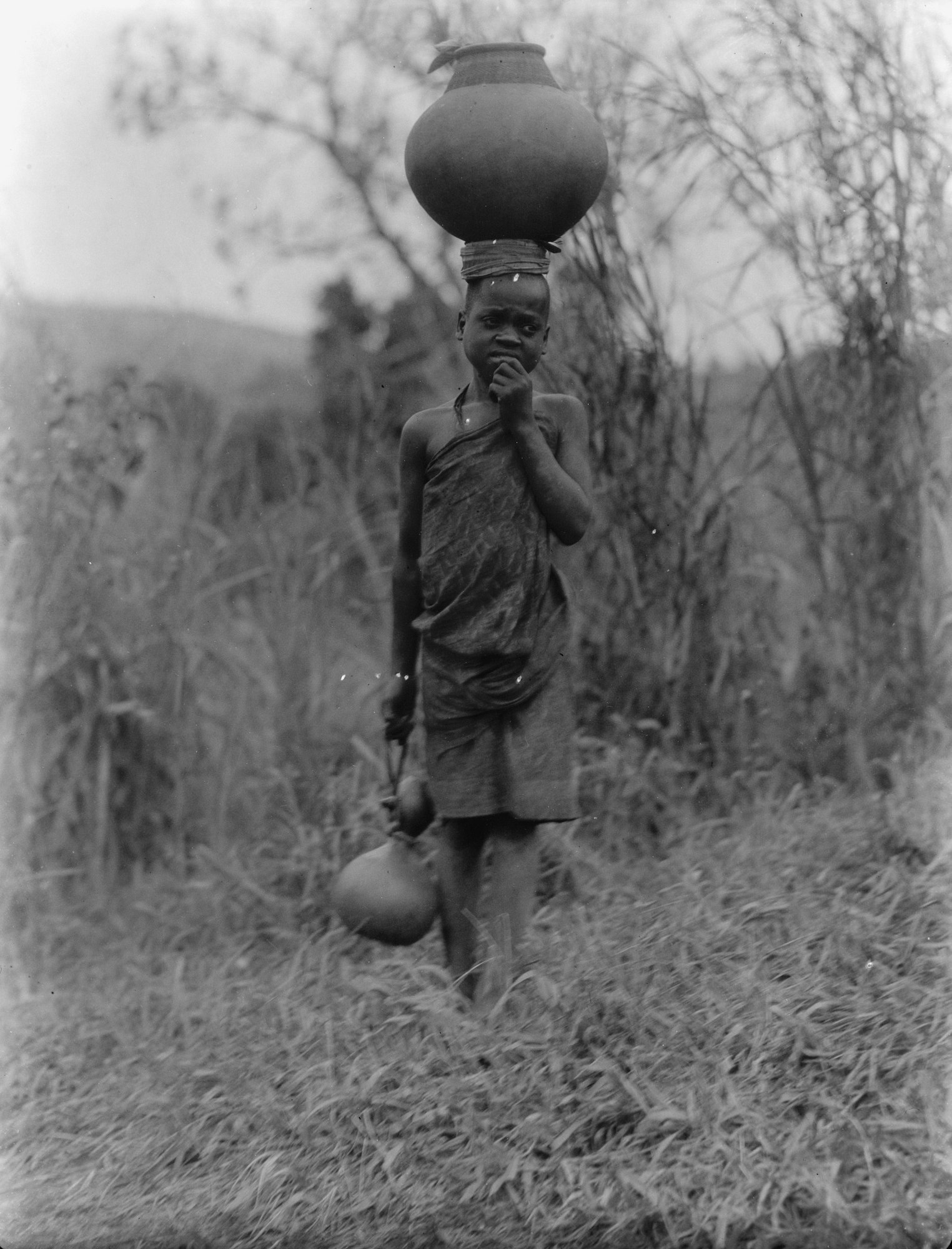 Black and white photo of a young man carrying water jugs