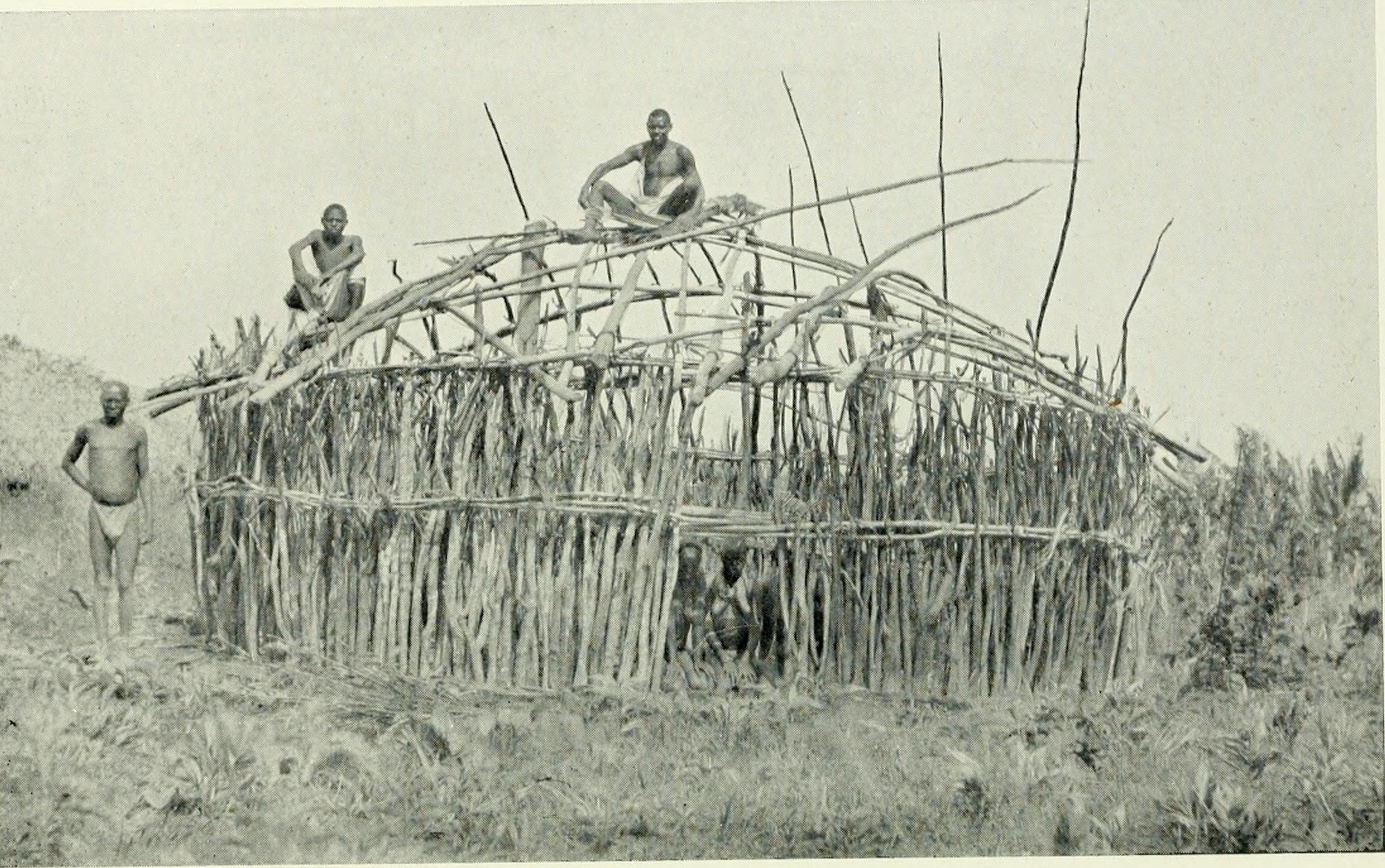 Black and white photo of men sitting on wooden house framing