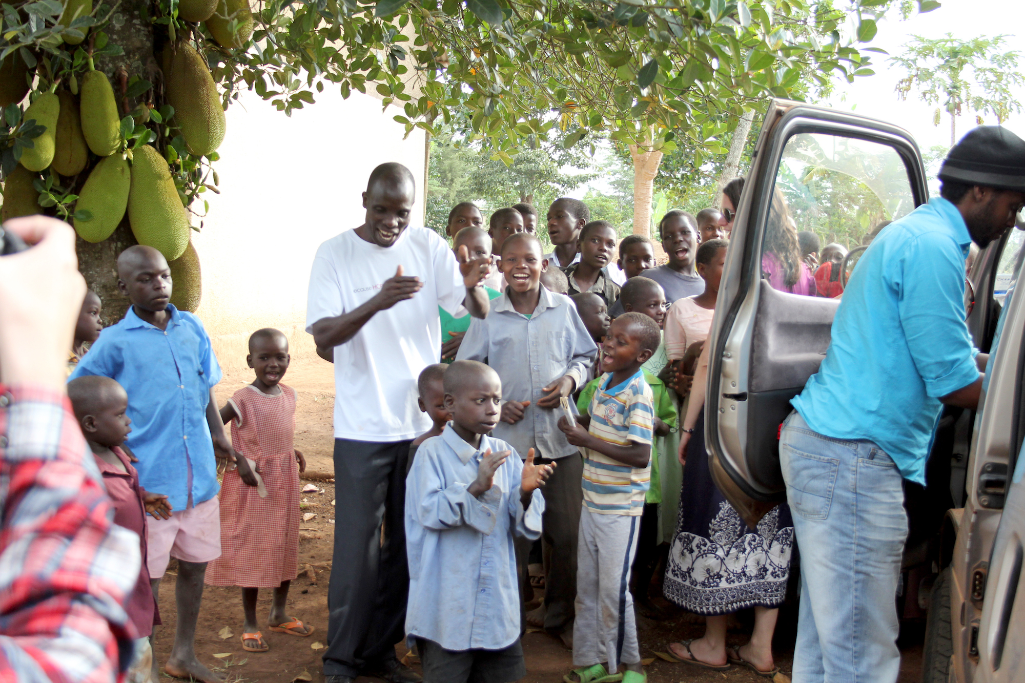 A group of children & men standing around an open car door